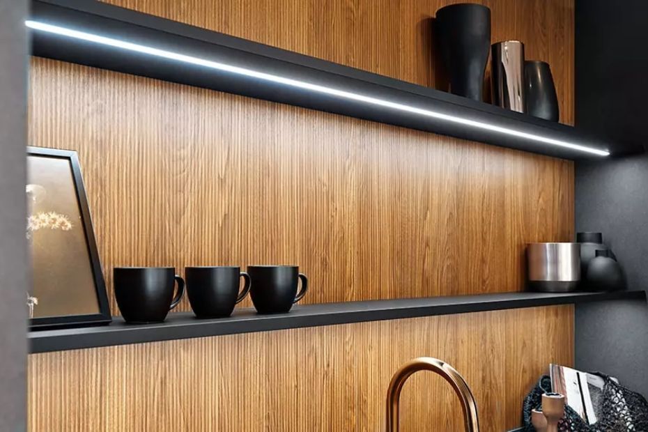 Detailaufnahme eines Regalsystems mit LED-Beleuchtung, Holzrückwand und schwarzen Accessoires.