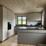 Helle Küche mit Kücheninsel, Holzdecke und hellen Fronten