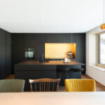 Minimalistische schwarze Küche mit Kochinsel, Barhockern und indirekter Beleuchtung